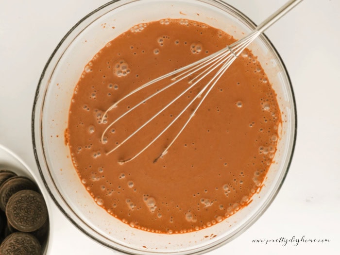 Mixing chocolate pudding in a large clear glass bowl for Easter dirt cups,