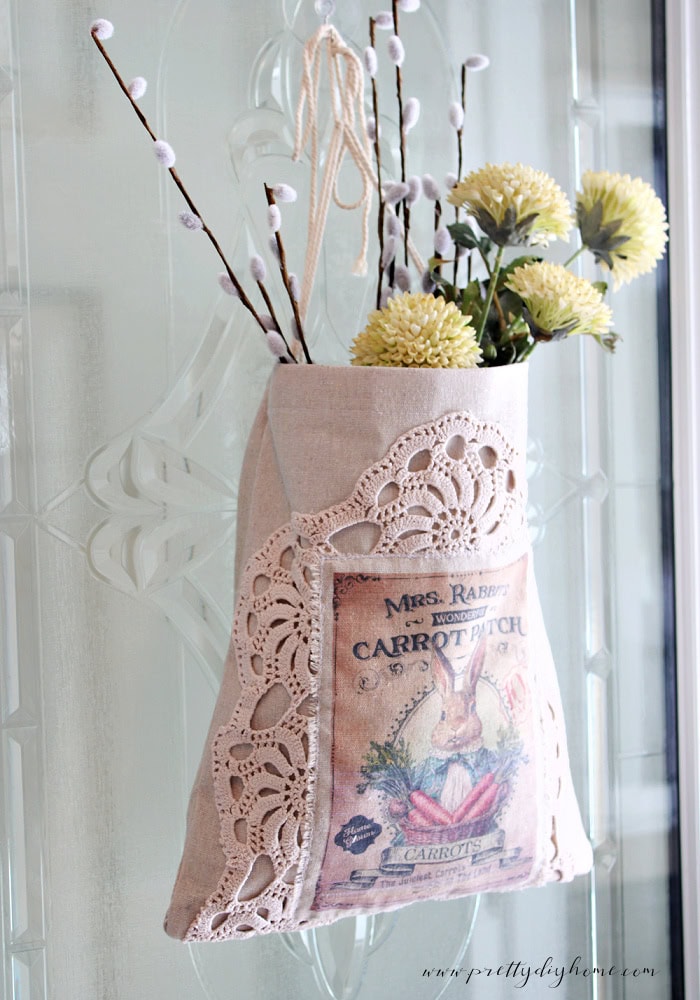 Linen bunny wall pocket hanging on a front door as a DIY spring wreath alternative.