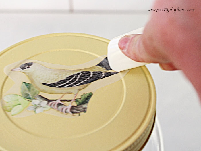 Closeup of applying bird transfer to painted jar lid using a plastic tool