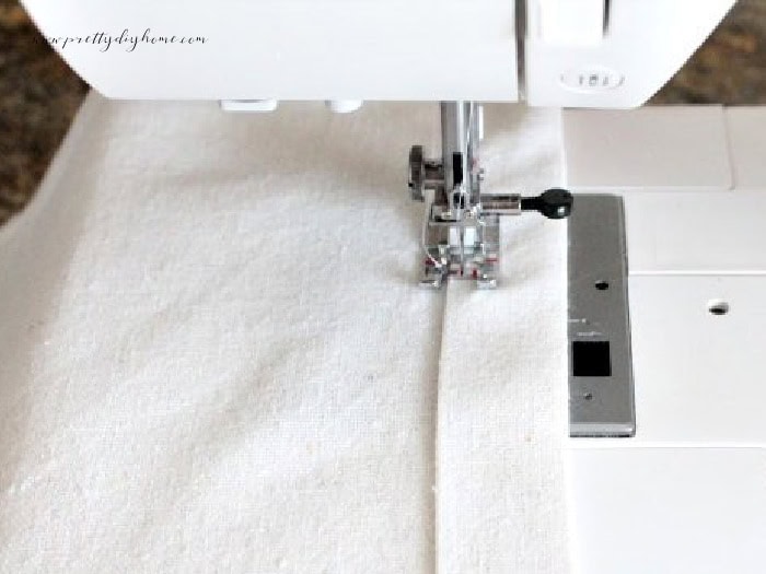 Sewing the folded top hem of the linen panel on a sewing machine for the DIY bunny wall pocket.