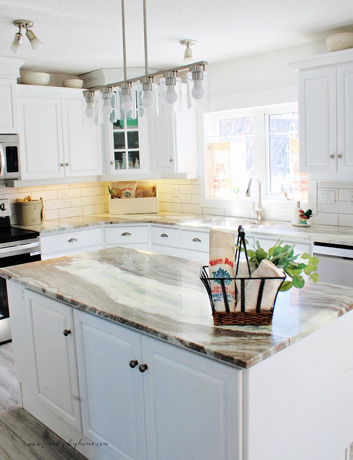 Vintage flour sacks styled in a white cottage kitchen, decorating an organizer, filling a basket, and used as curtains over the kitchen sink.