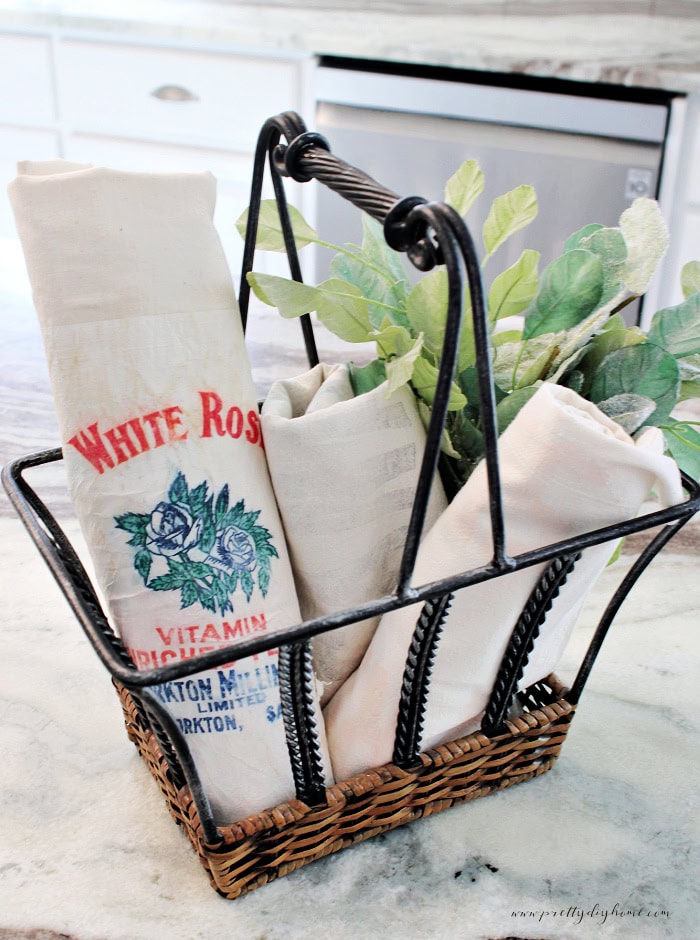 Vintage flour sacks rolled in wire basket with lambs ear greenery.
