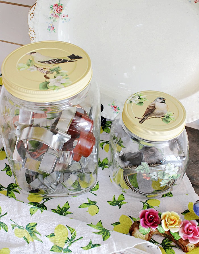 Vintage glass jars with painted lids and bird transfer designs used for kitchen storage.