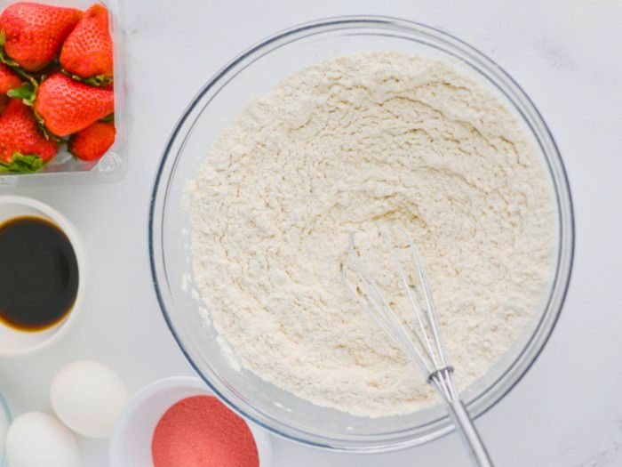 Mixing dry ingredients for strawberry slab cake in a bowl with a whisk.