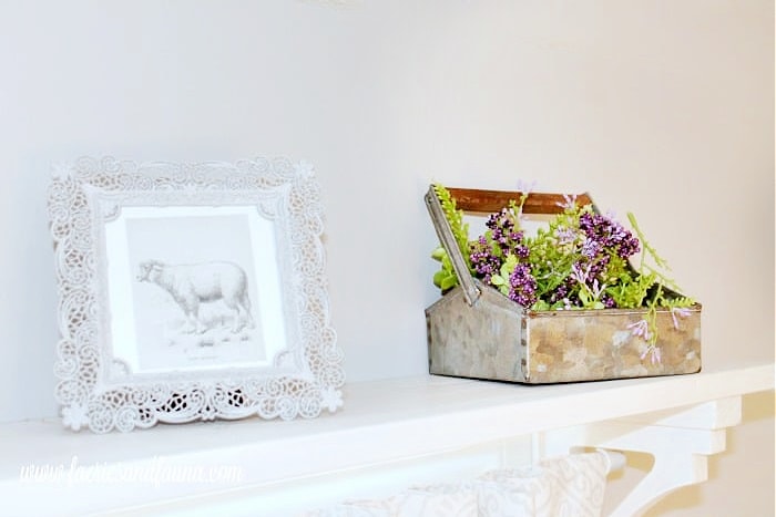 Two small pieces of farmhouse decor, one is a small picture frame, and the other is a small galvanized container holding greenery. The two accessories are sitting ontop of a DIY window shelf curtain rod combo made from wood and painted white.