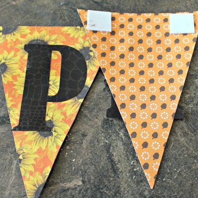 Attaching scrapbook paper to burlap in a fall pumpkin banner craft project for fall.