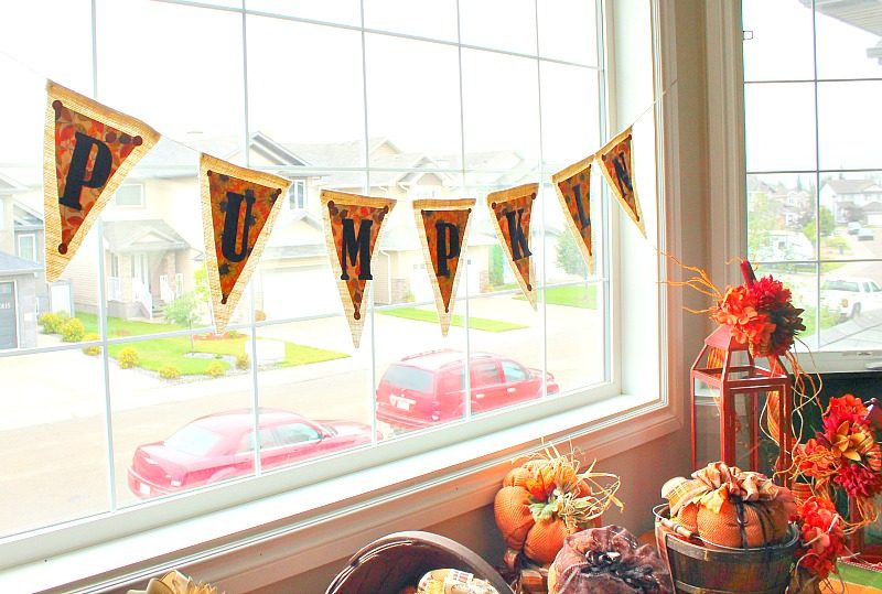 A large front window display for fall with a handmade fall pumpkin banner.