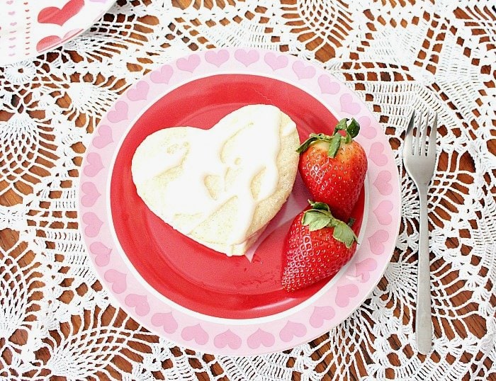 Strawberry Valentine dessert recipe or ice cream sandwich recipe being served on a Valentine themed plate with two fresh strawberries on the side.  The background is a lace tablecloth.