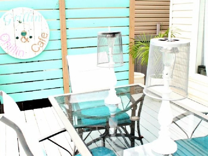 Two white DIY solar lamps sitting on a patio table with bright turquoise accessories.