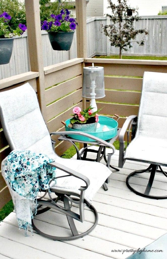 This painted patio chair seating area shows the finished chairs in the corner of the deck, surrounded by plants and teal decor.