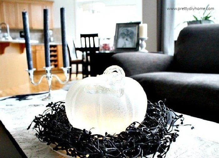 A white sparkling Halloween pumpkin glowing with lights while sitting on a bed of black sparkling beads.