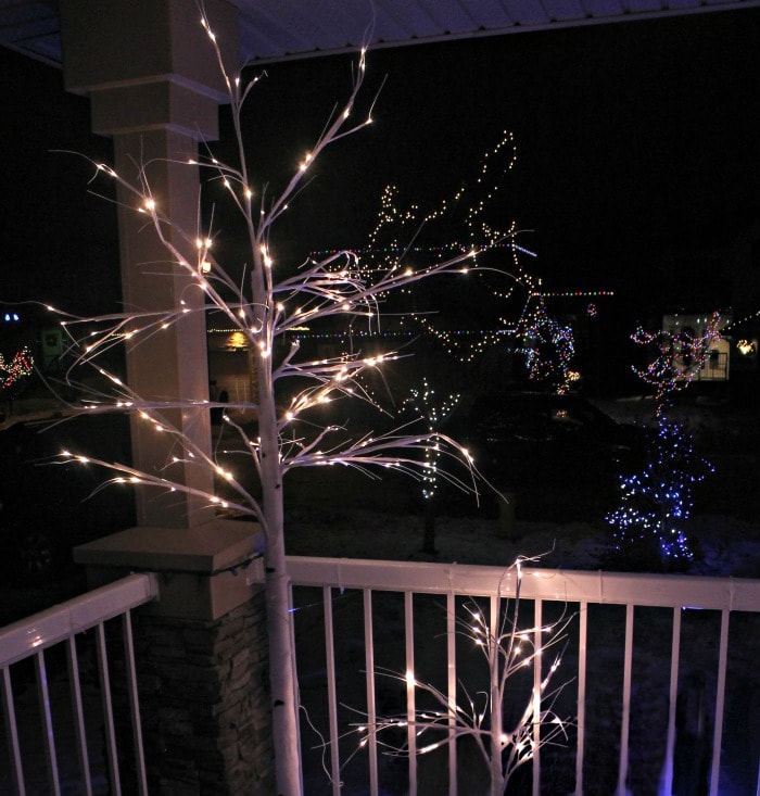 Exterior christmas decorating idea lighting up a Christmas porch with all kinds of pretty Christmas trees with white sparkly branches.