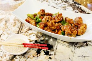 A oblong dish full of battered pork thats smothered in a homemade sweet and sour sauce. There are also green pepper and carrots in the sauce.