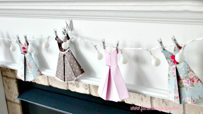 Folded scrapbook paper turned into vintage dresses and hung on lights for a banner. Perfect for wedding showers, or little girls room. origami dress, DIY paper banner, paper dress banner, paper dress design, spring banner, DIY spring decor, paper home decor, paper dress, banner