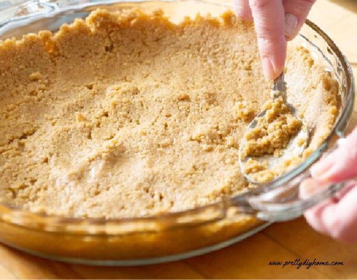 Pressing a graham cracker crust into a pie plate using a spoon to get the crumbs on the sides of the pan.