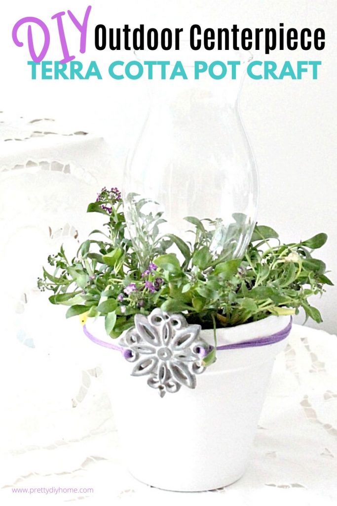 A Dollar store clay pot is painted white and given a glass lantern top with flowered plant to create an outdoor centerpiece.