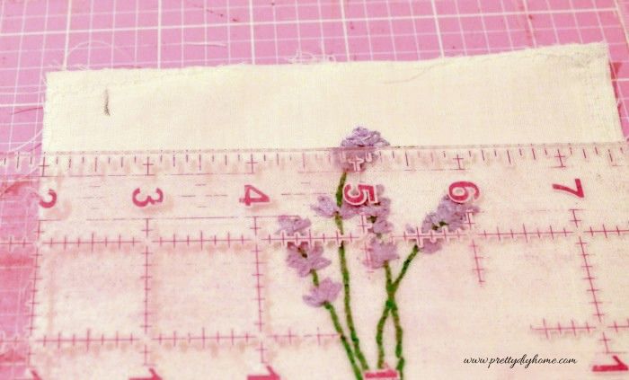 Measuring fabric from the center of a lavender embroidery design with a ruler.