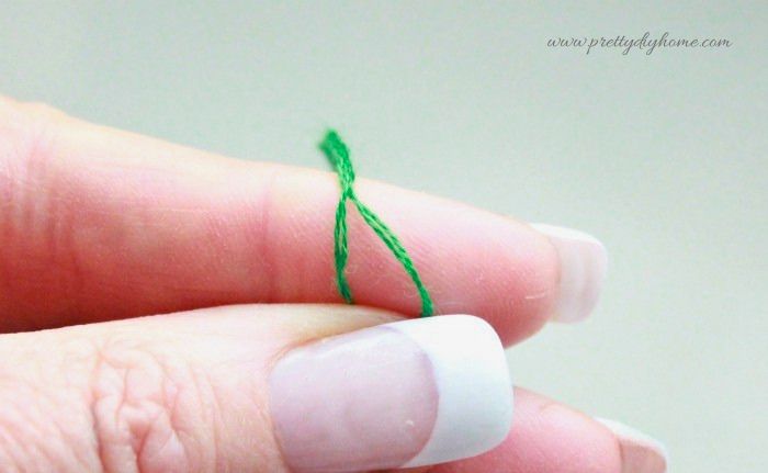 Hand separating green embroidery floss into two strands for stitching