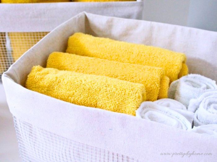 A fabric liner is folded over the edge of a wire basket and filled with neatly arranged towels.