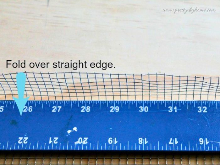 Folding wire over a straight edge to fold down the top of the wire mesh to create a smooth edge for a basket.