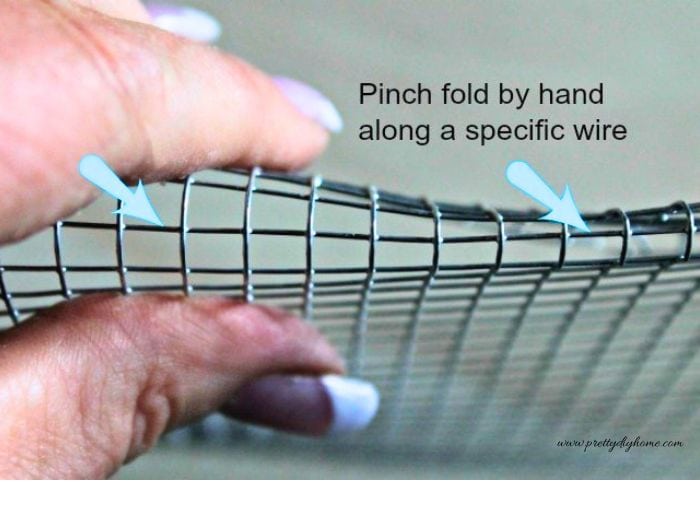 The folded edge of the wire mesh is pinched by hand to create a clean, smooth edge for the basket.
