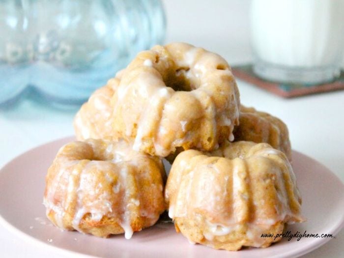 A small pink plate covered with homemade baked pumpkin donuts in a small stack.  The pumpkin donuts are golden orange with a clear glaze on top.