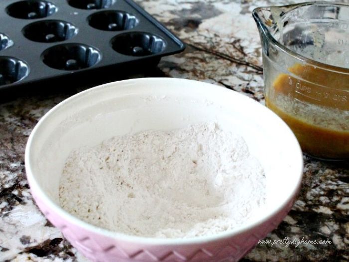 A large mixing bowl filled with the dry ingredients for pumpkin donuts. There is a baked donut pan in the background.