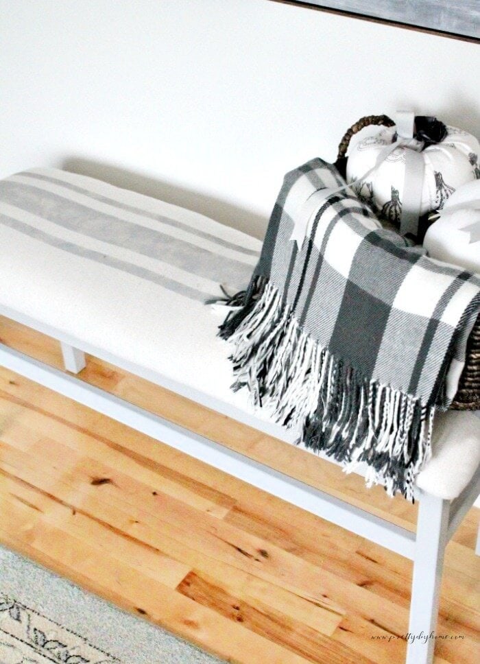 A upcycled DIY bench with new DIY bench upholstery.  The upholstery is done in grey grainsack stripes painted onto dropcloth fabric.