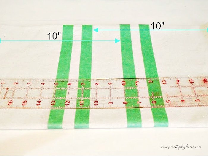 Placement and measurements of green painters tapes with markings and ruler illustrating where to tape and paint stripes onto dropcloth.