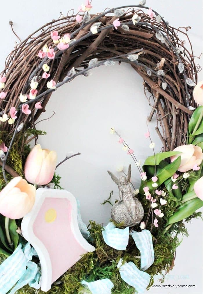 A large fairy wreath diy for Spring. An easy to make Spring wreath DIY with tulips, green moss, small pink flowers, a pretty fairy door, colorful ribbon and a beautiful fairy.