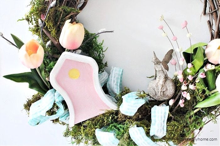 A whimsical fairy wreath for Spring with soft pink tulips, small piunk blossoms, blue checkered ribbon, soft green moss, a beautiful pink fairy door and a pretty fairy.