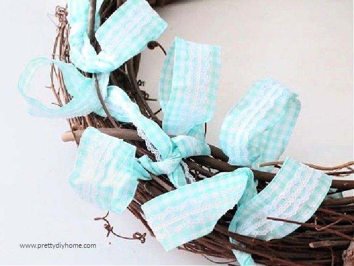 Four loops of checkered blue cotton ribbon with lace, being attached to a grapefine form while making a fairy wreath for Spring.