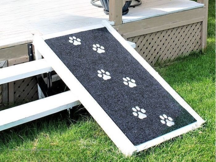 Finished DIY dog ramp installed over outdoor stairs, painted white with black carpet and white painted paw prints.