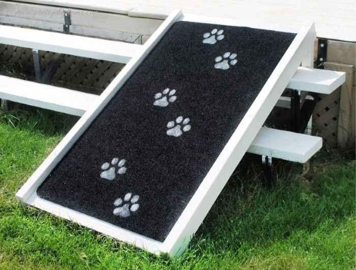 Finished DIY dog ramp over stairs with painted paw print design on black carpet surface.