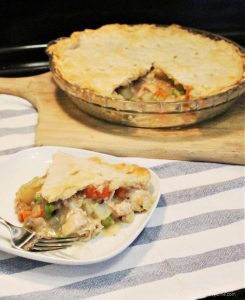 Chicken pot pie with a slice out of it in the background. The foreground has a slice of pie showing chicken, carrots, peas and sauce.