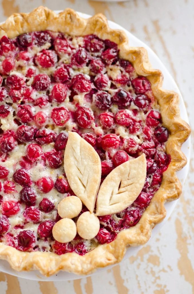 A whole cranberry orange custard pie. The pie is decorated with leaves and three balls of pie crust to resemble holly.