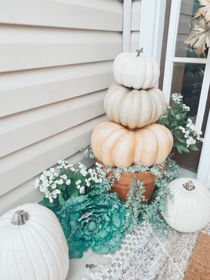 A neutral and green Fall porch with pumpkins, green plants and a cabbage leaf plant.