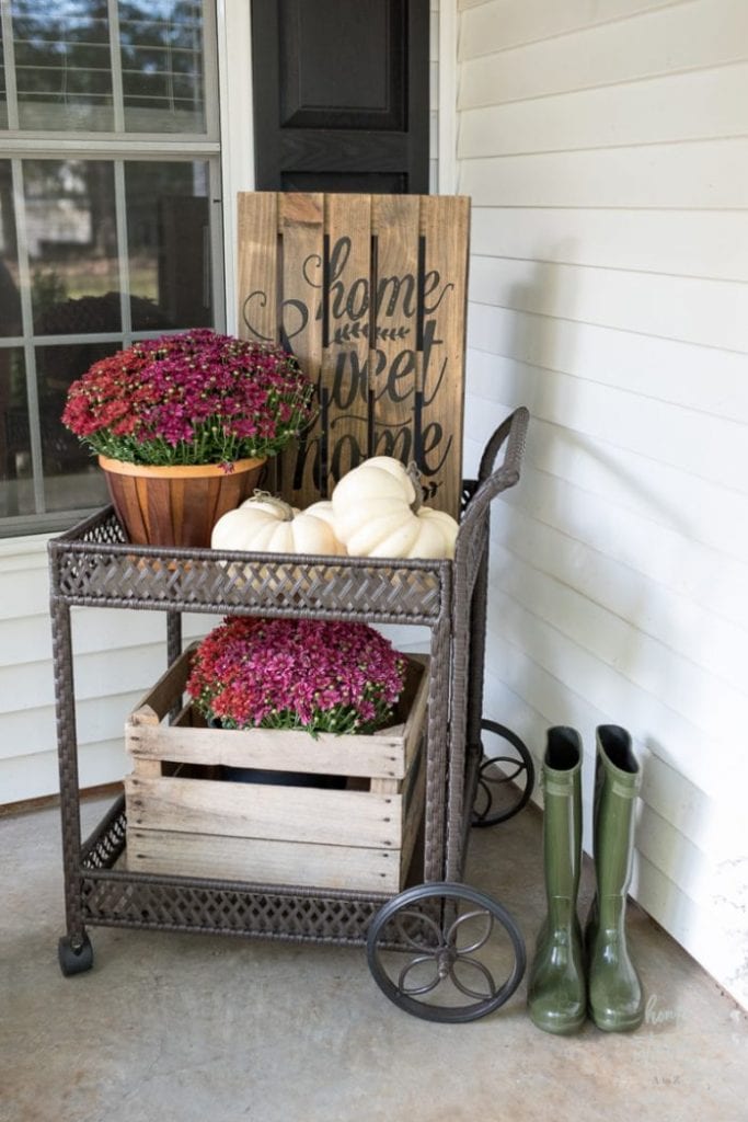 A beautiful decorated porch corner with purple mums, white pumpkins a farmhouse home sweet home wood sign and a pallet box. Its tha beautiful fall decor idea for a small space.