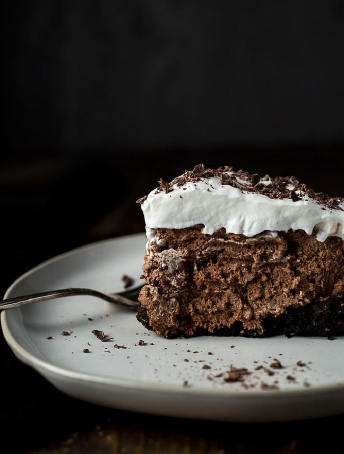 A very thick piece of chocolate mousse pie. This pie recipe is no bake. The pie is very thick with whipped cream on top. The background is black.