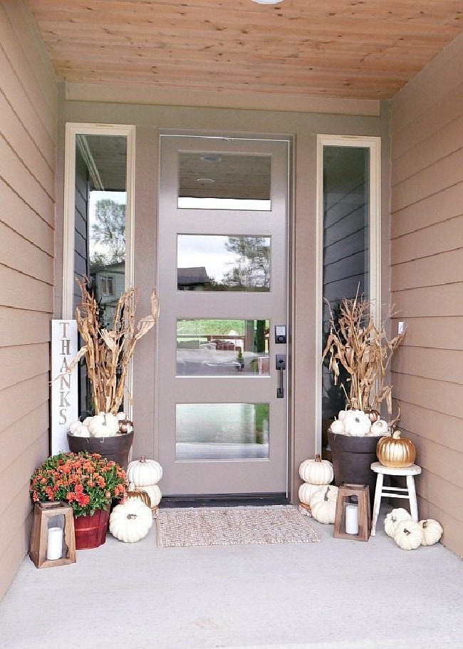 Metallic front porch decor with mettalic and white pumpkins, a traditional orange Mum, wooden lanters, and corn stalks.