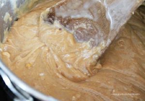 A saucepan with melting peanut butter being stirred with a large wooden spoon. Making no bake peanut butter square Christmas recipe