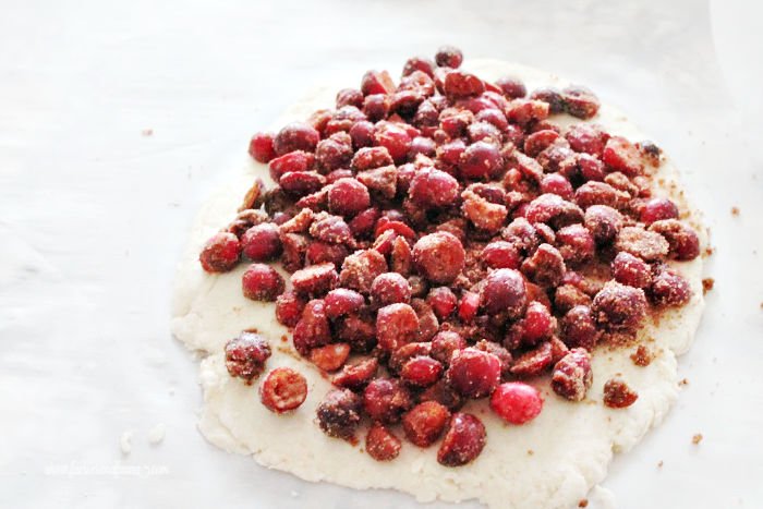 Cinnamon and sugar coated cranberries piled on top of scone dough while make a cranberry scone recipe.