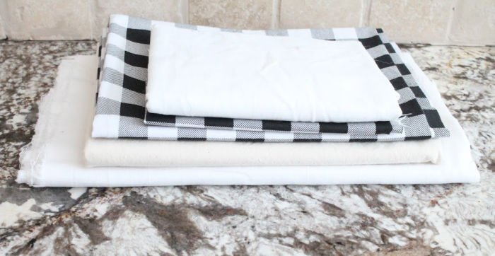 A stack of farmhouse fabrics including buffalo check for making a stuffed farmhouse Easter bunny craft.