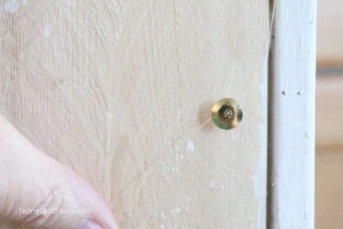 Using tacks to attach fishing line to the back of a DIY Farmhouse shiplap backdrop for Easter decorating