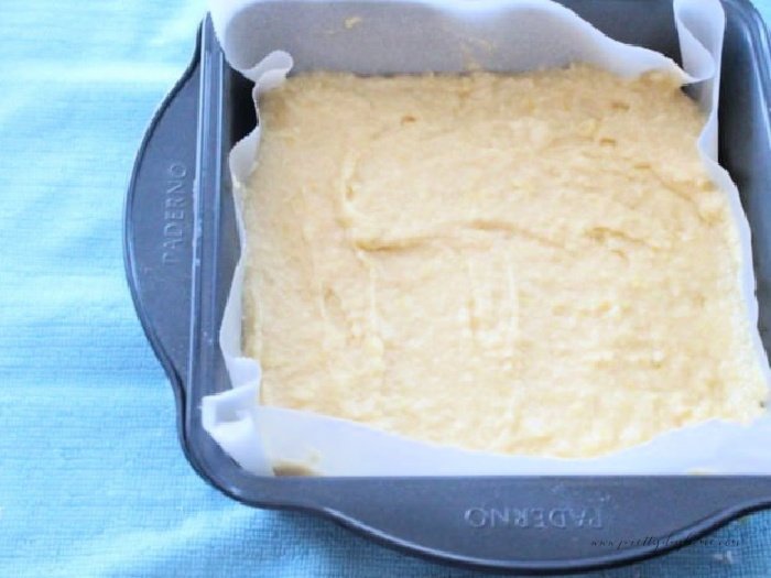 A parchment lined square baking pan filled with lemon bar batter.