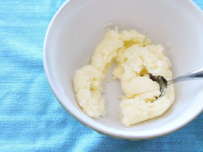 Butter and sugar being blended together with a spoon in a small white mixing bowl.