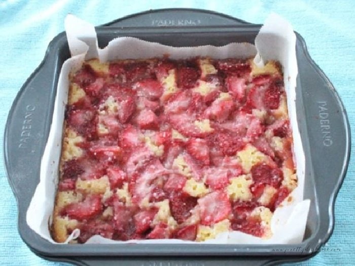 A pan of freshly baked lemon bars with strawberries cooling on a counter.