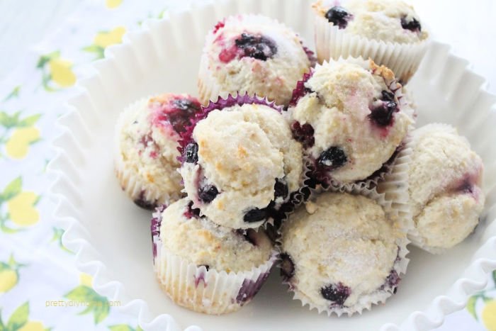 A bowl full of pretty blueberry lemon muffins in a white bowl. They have a light dusting of white sugar on top.