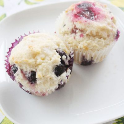 A plate with two delicious lemon blueberry muffins with a whtie streusel topping.