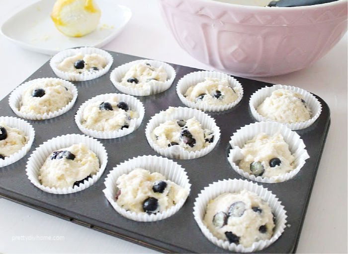 A muffin tray with 12 blueberry lemon muffins before baking.